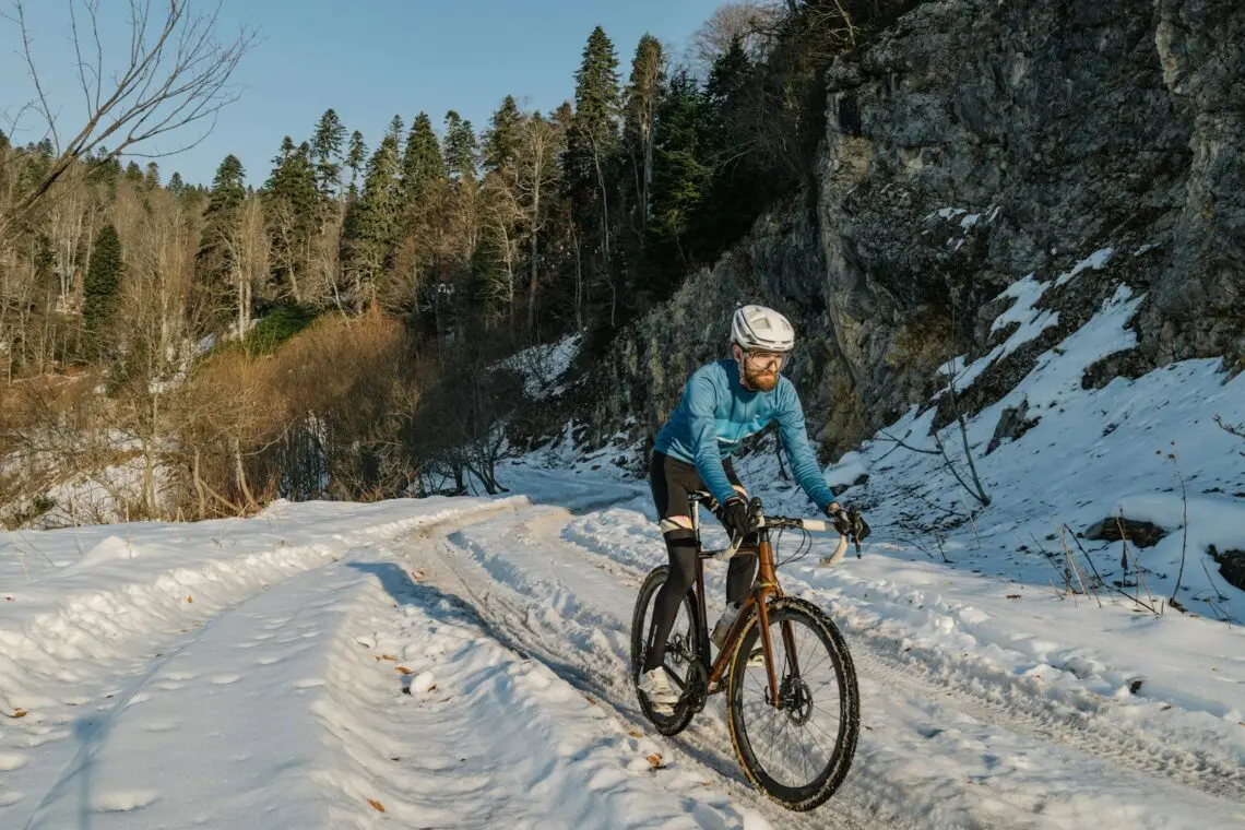 Cycliste en tenue thermique roulant sur une route enneigée en hiver