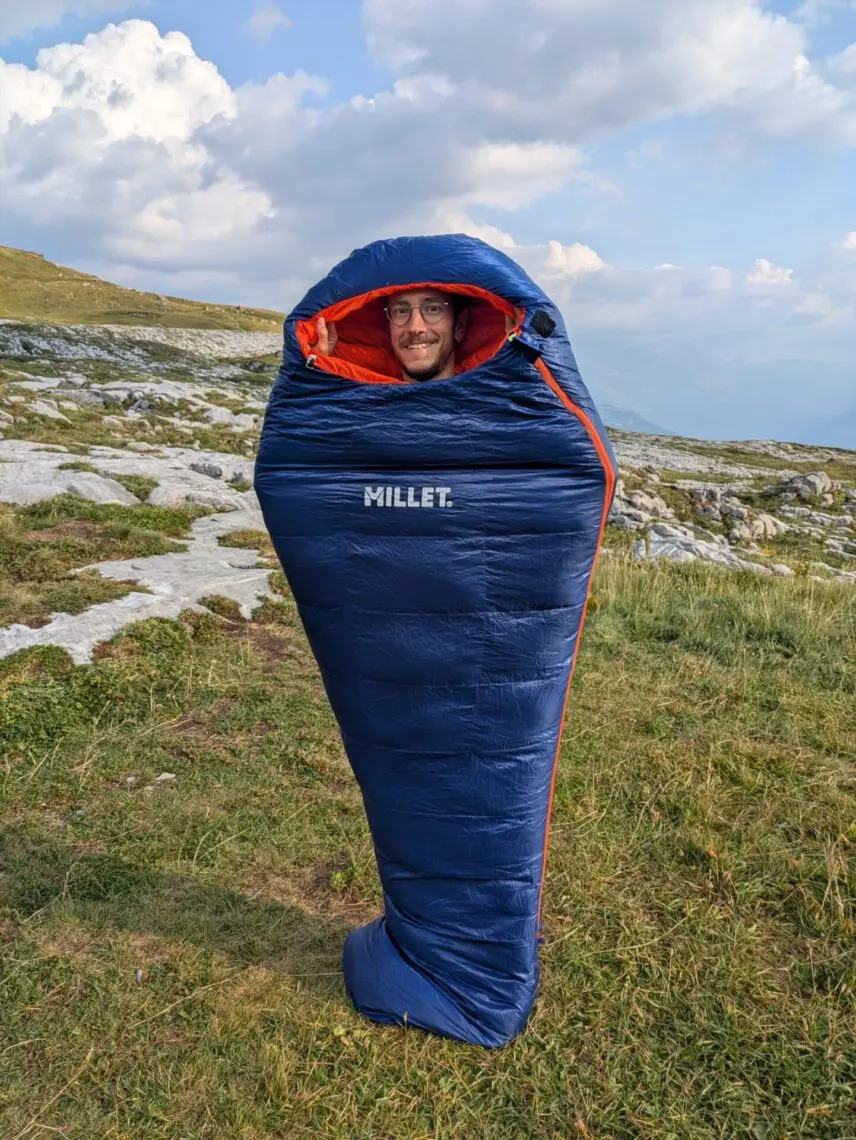 Cycliste dans son sac de couchage en duvet au bivouac, en montagne