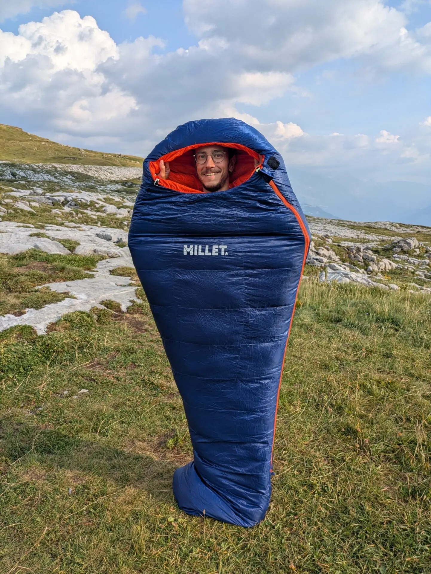 Cycliste dans son sac de couchage en duvet au bivouac, en montagne