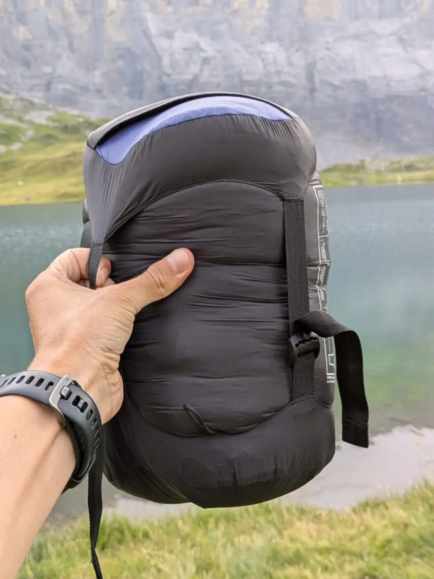 Sac de couchage rangé dans son sac de compression, tenu à la main