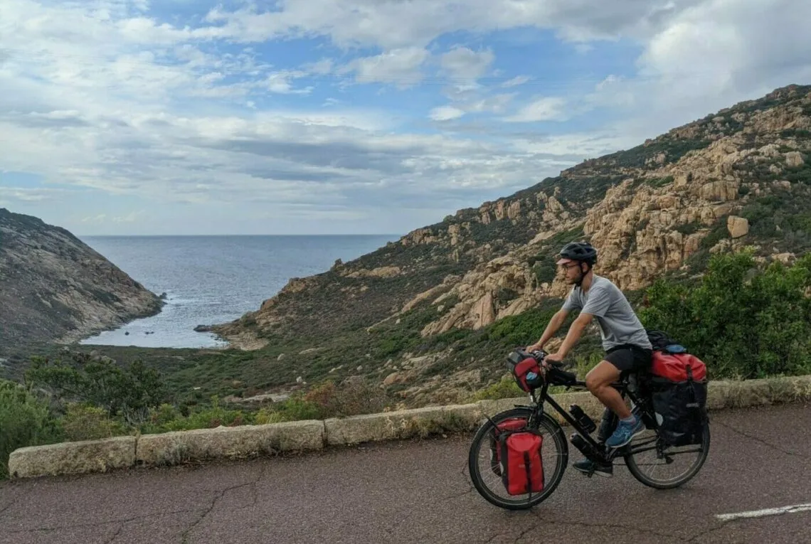 Vélo de voyage chargé avec ses sacoches avant sur la route côtière du golfe de Porto, en Corse