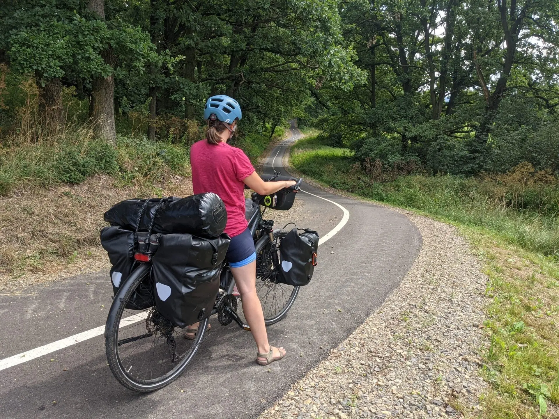 Velo de voyage charge vu de dos sur une piste, sacoches arriere et sac sur le porte-bagage