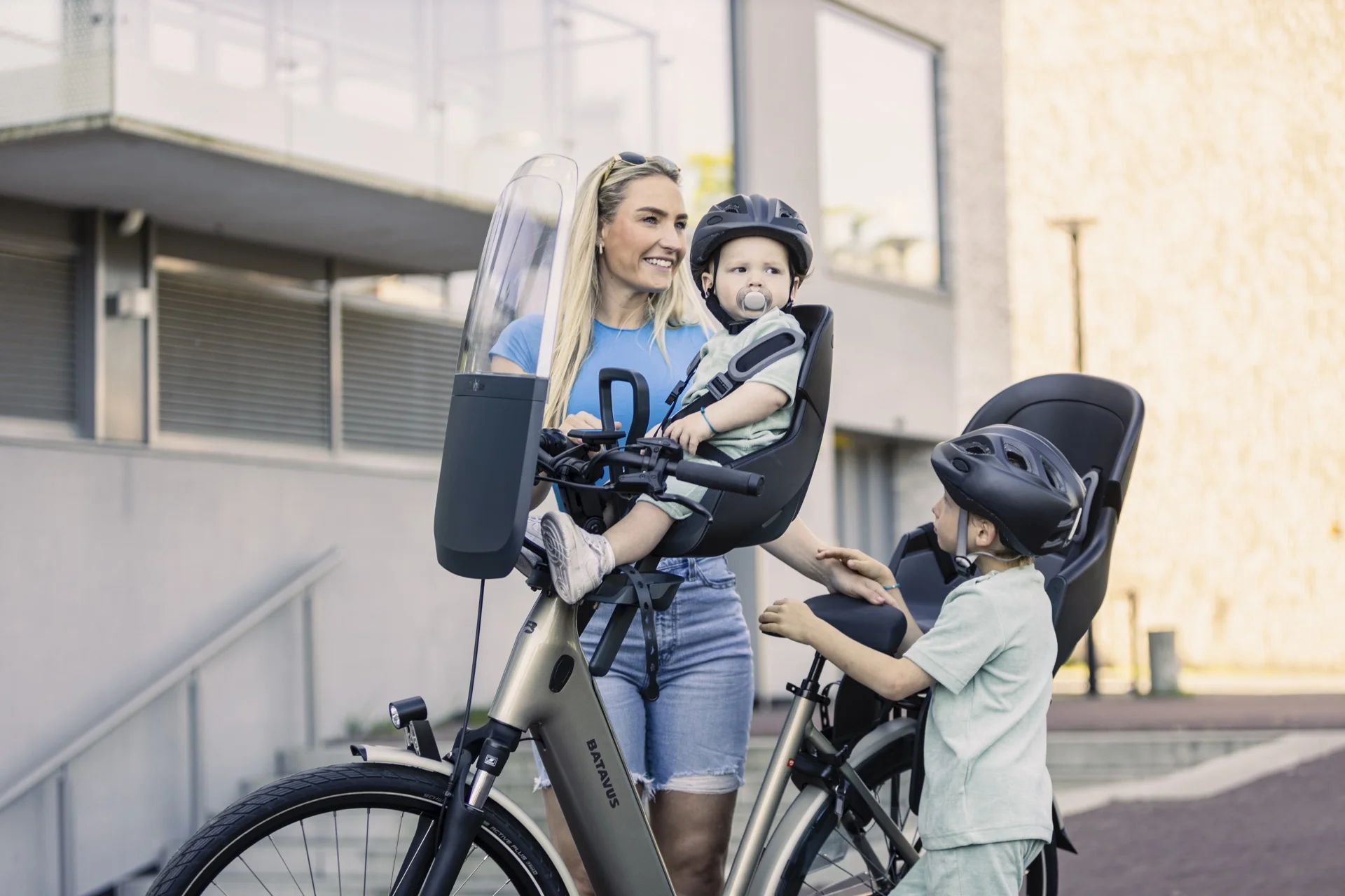 Enfants casqués autour d'un vélo équipé d'un siège bébé avant et d'un siège arrière