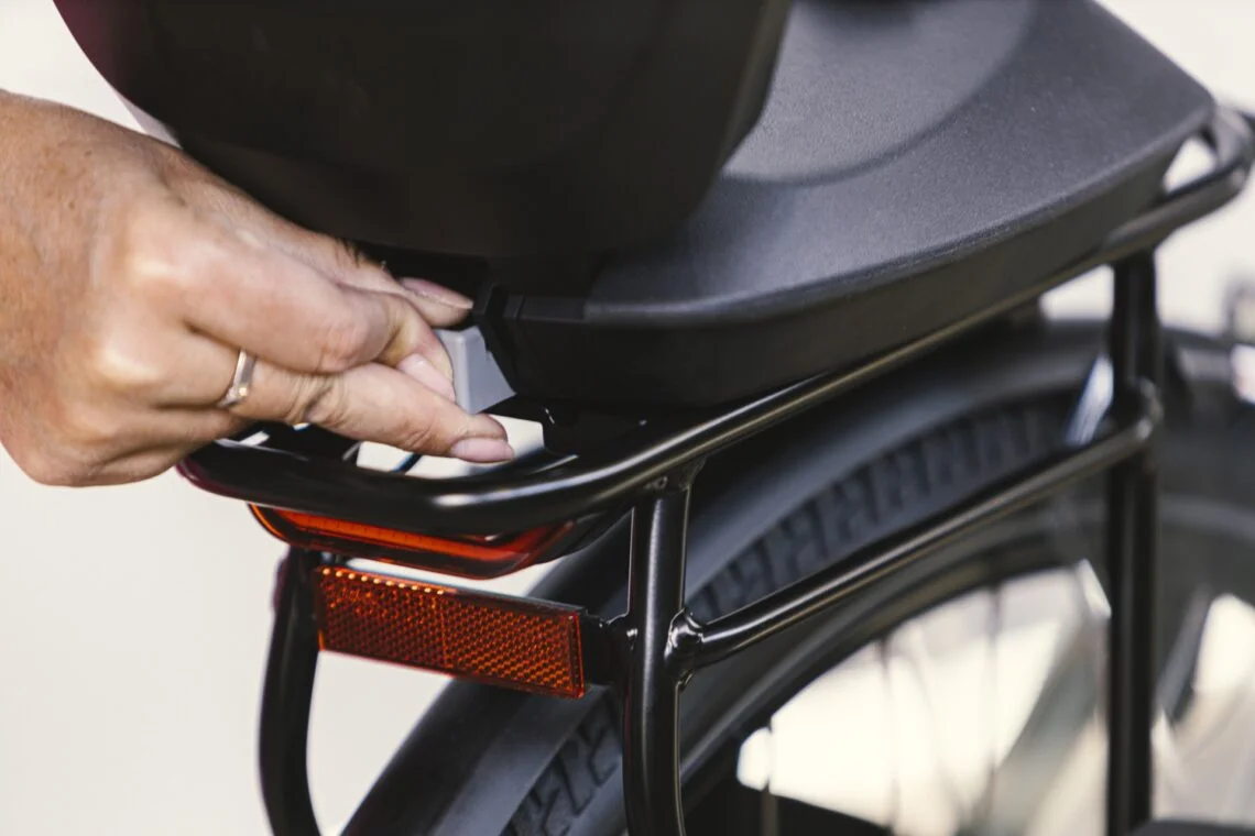 Main qui verrouille la fixation d'un siège vélo bébé sur un porte-bagages